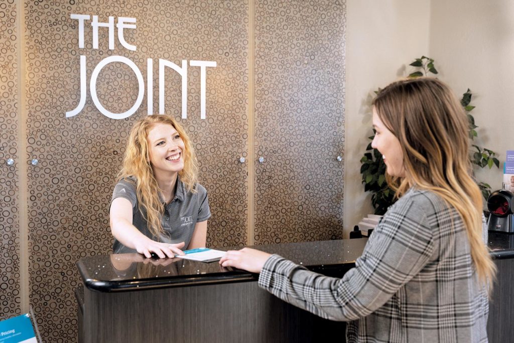 The Joint Chiropractic Franchise receptionist hands paper to patient